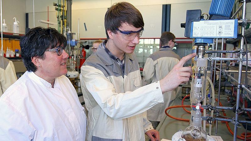 Linus Busse, Teilnehmer der Internationalen Chemieolympiade, erläutert der Landesbeauftragten Birgit Vieler die Besonderheiten einer Apparatur für die Wirkstoff-Synthese.